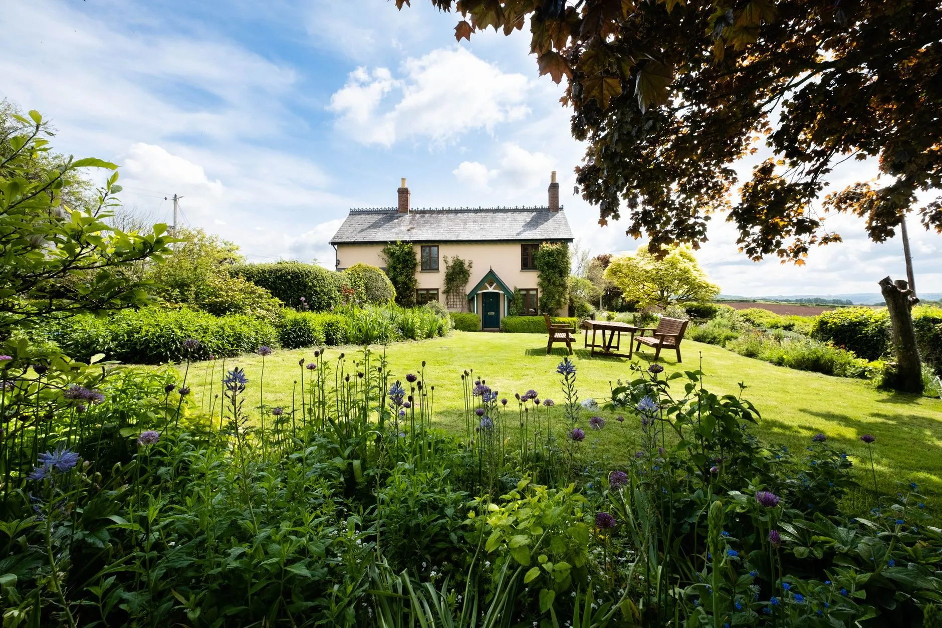 A cream farmhouse seen across a summer garden and lawn