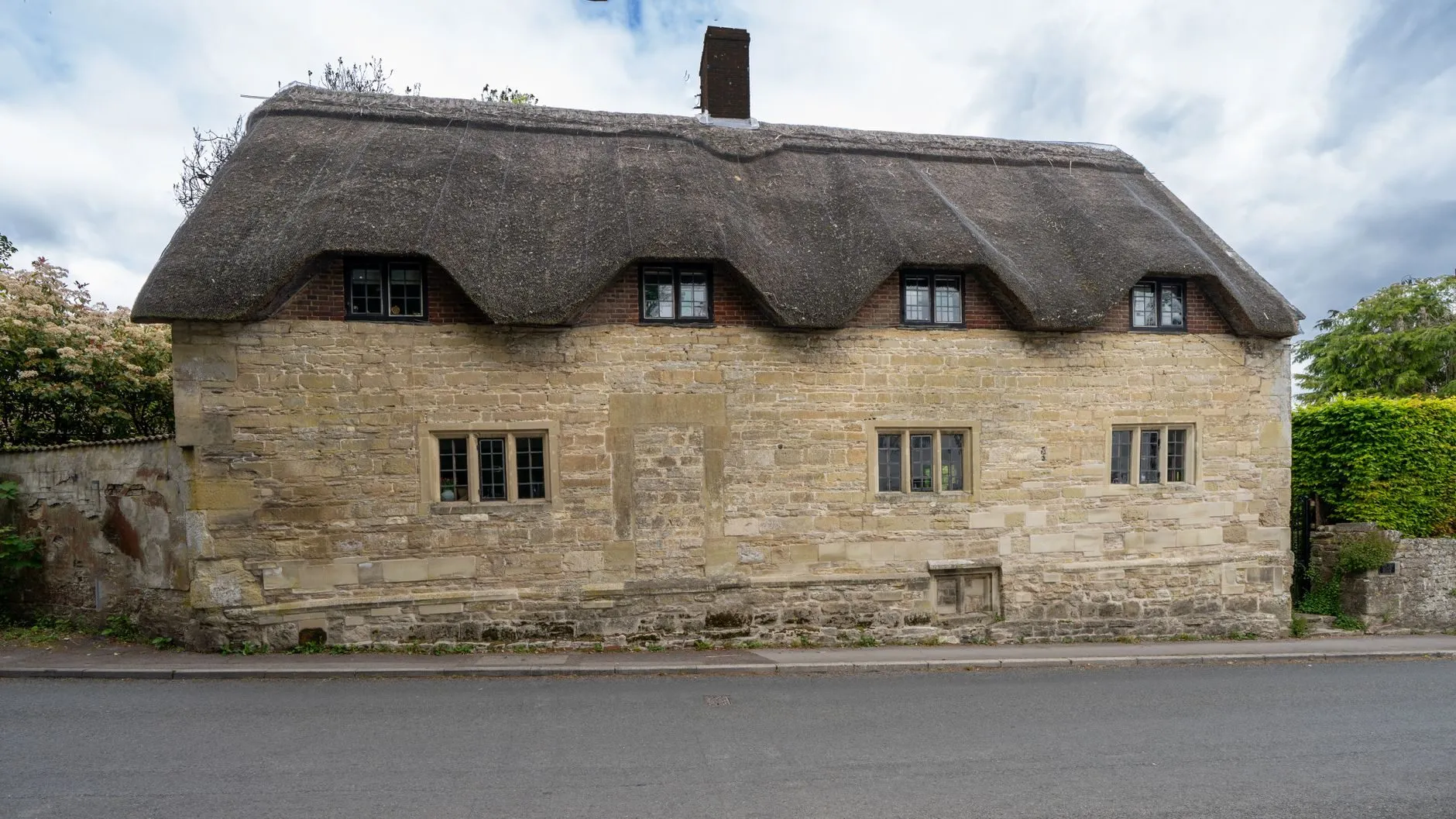 A stone cottage with a deep thatched roof beside a village road