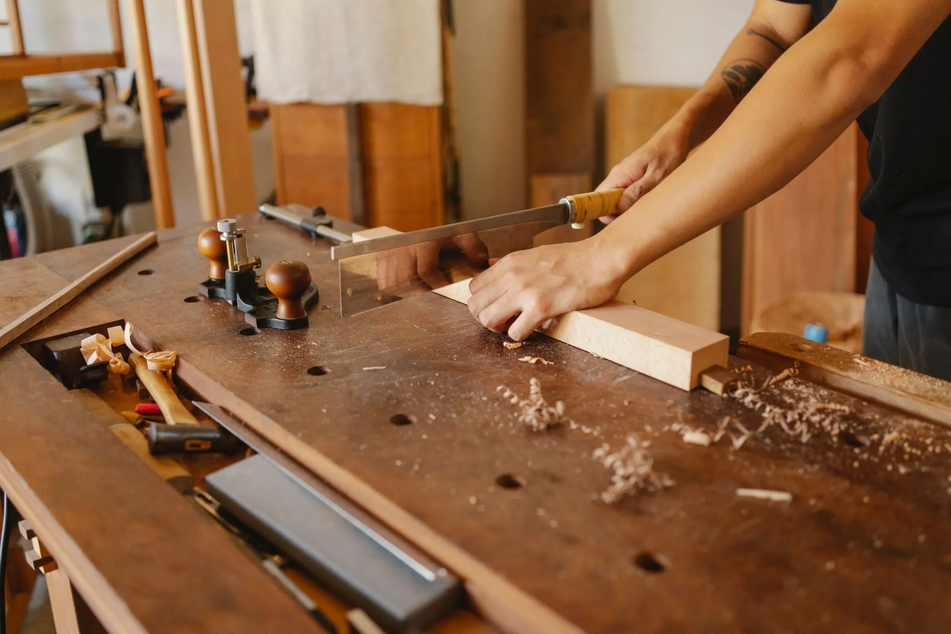 A joiner cutting timber with a pull saw on a workbench scattered with shavings